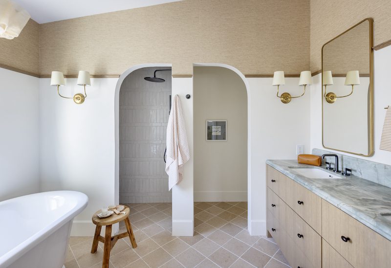 custom ensuite with double sconces on either side of the single arched doors with ceramic tile floor and clawfoot bathtub and double vanity