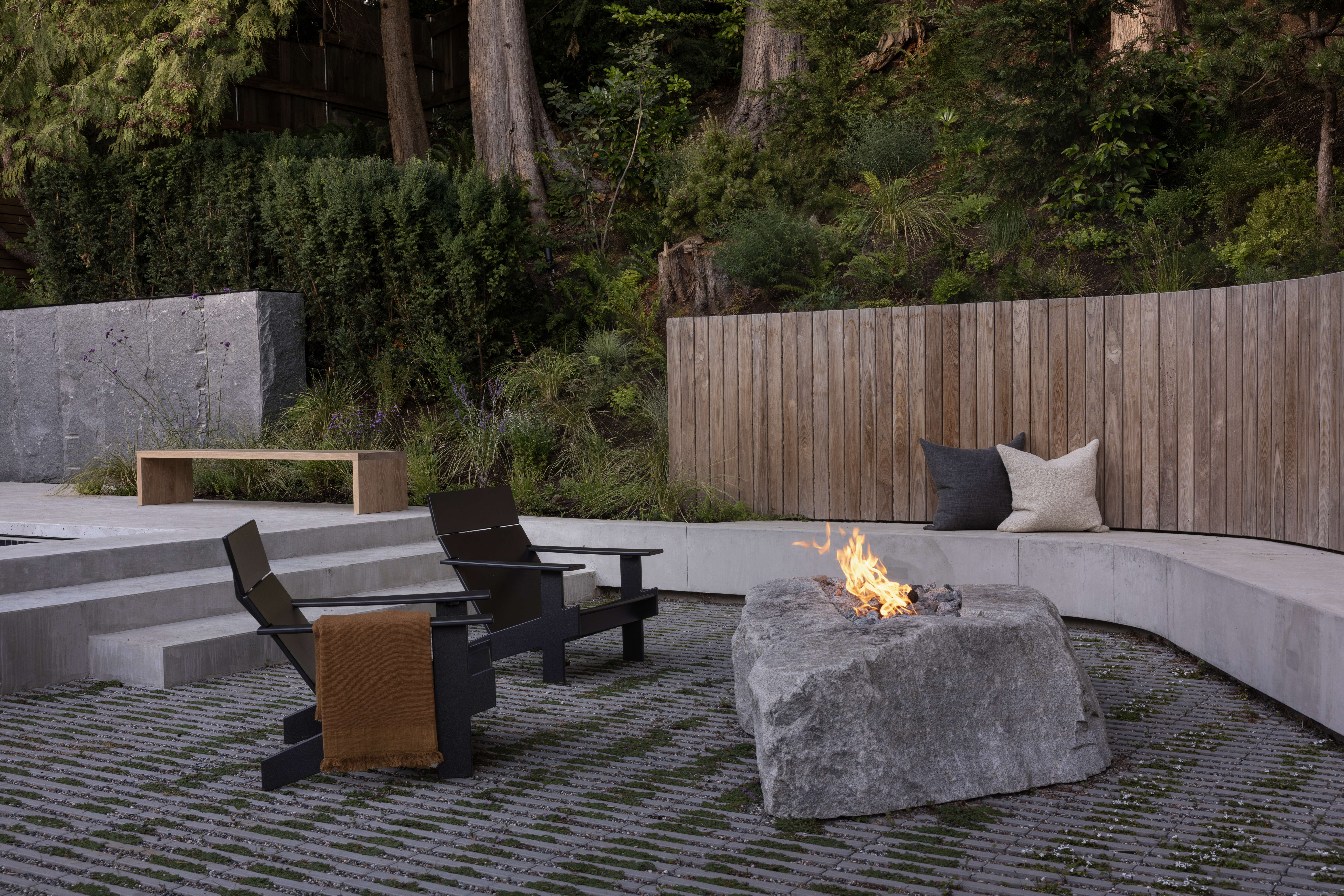 Outdoor seating area with custom stone fire pit beside pool at Japandia residence